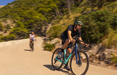 Actor portrayal of man and woman biking on a road with bushes behind