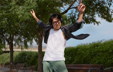 Actor portrayl of an adult male dancing with his arms raised wearing black headphones